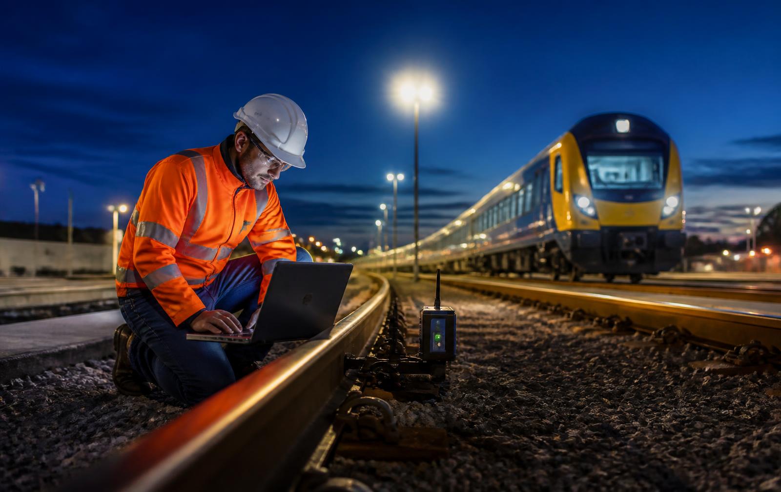 Rail engineer on a test track at night with a laptop beside a wireless sensor node mounted to the rail